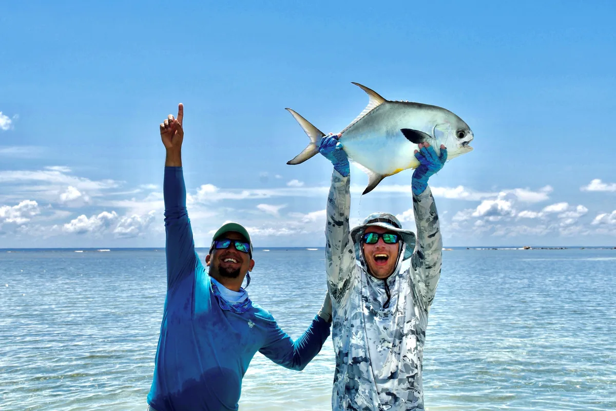 Two anglers in the shallows lifting a permit overhead